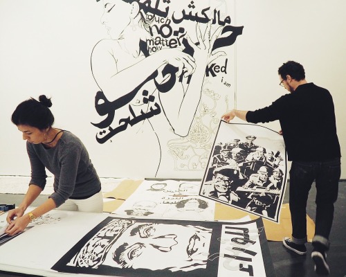 Conservators and preparators work to install a wall of graphic material by Egyptian graphic artist, 
