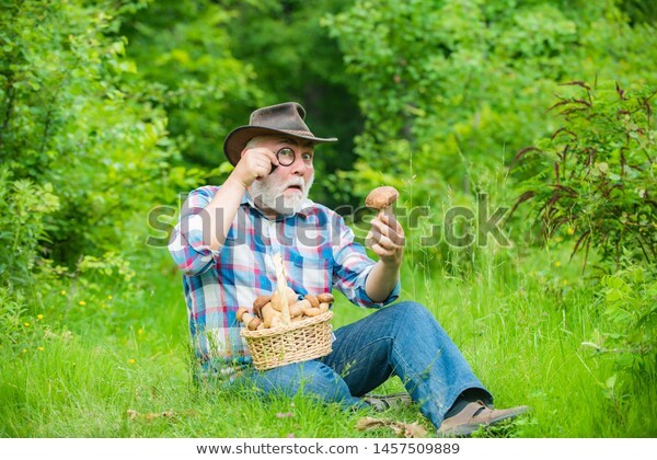 Old bearded man with a monocle, looking in astonishment at a mushroom. 