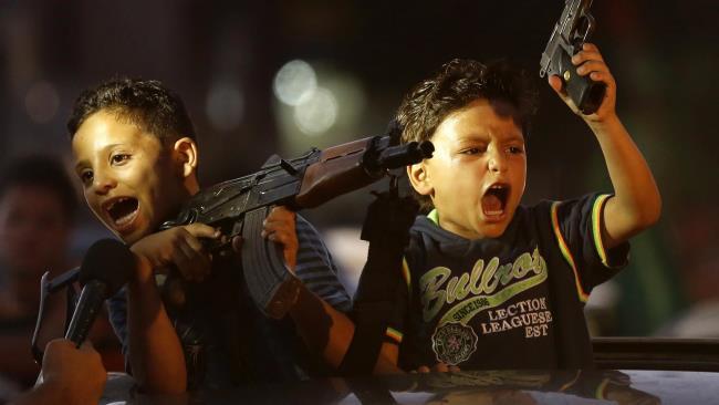 politics-war:  Children hold up guns, one with an empty magazine, from a car as Palestinians