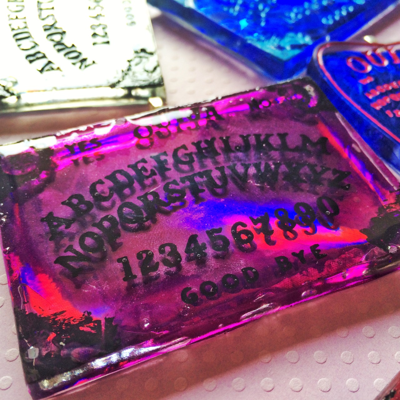 jinxandcurses:  NEW! Holographic ouija boards in planchettes in pink, purple, blue,