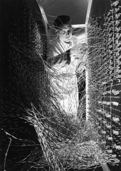 historicaltimes:  A male technician stands and adjusts the wiring at the rear of a large computer designed to monitor water depth and soil quality in Phoenix, Arizona, 1965 via reddit 