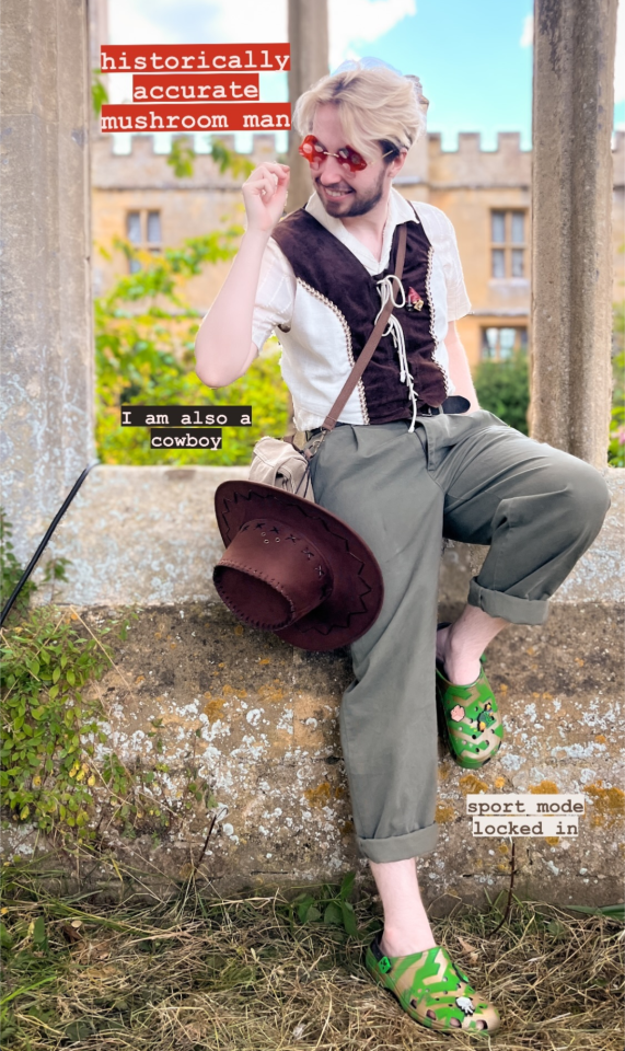 A selfie of Oli TheOrionSound, from his Instagram story. He is a young white man with bleach-blonde hair. He is dressed in a combination medieval and cowboy outfit, and is wearing modern red mushroom sunglasses. A cowboy hat is hanging from his bag, and he is wearing green and gold crocs. He is posing against a wall and smiling.
The captions read "historically accurate mushroom man", "i am also a cowboy", and "sport mode locker in".