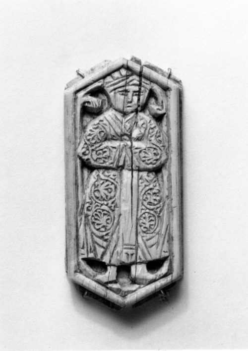 A hexagonal ivory furniture inlay with the figure of a standing man in a coat, decorated with palmet