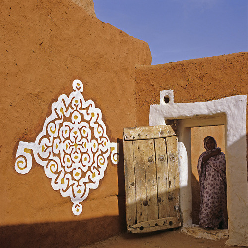 A woman stands in the doorway near a wall with hand-painted art. Hand painting, “vernacular art and 