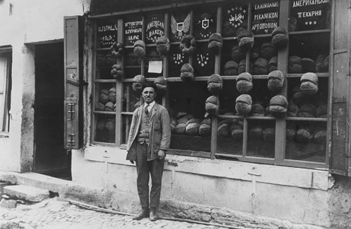 Baker standing in front of the ‘American Bakery’ which displays signs in Armenian, Ladino (in Hebrew