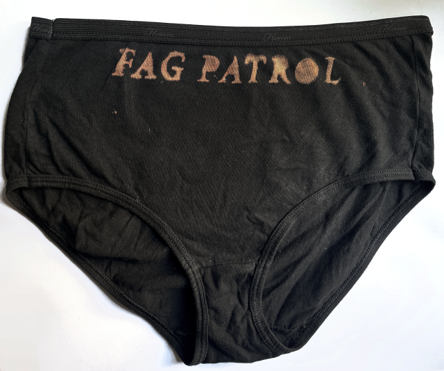 A photo of black underwear against a white background. The words "FAG PATROL" are painted in bleach under the waistband.