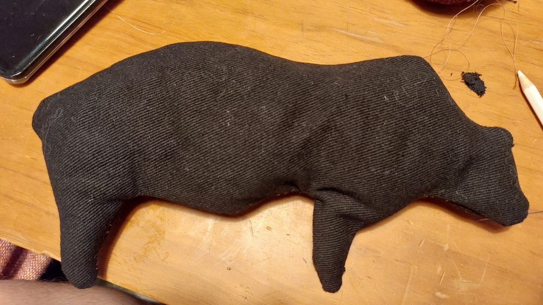 a photograph of a flat plushie made of black fabric on a wood table. the plushie has been made in the shape of a cave painting of a bear from the Chauvet Cave
