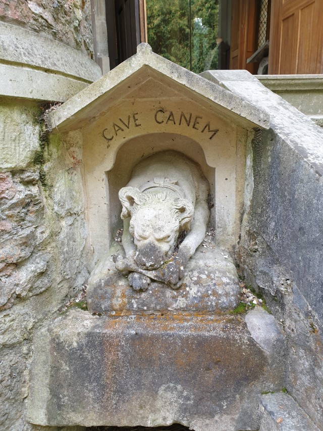 a stone carved dog's house with the inscription "cave canem" and a stone statue of a dog gnawing on a bone in it