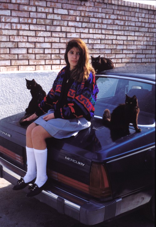 raunchily:Teen girl sitting on the back of a car with black cats in Juárez photographed by Mark Jay Goebel, 1988