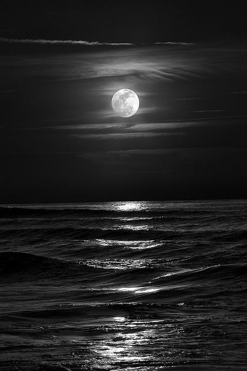 a black and white image of the moon reflecting on open ocean 