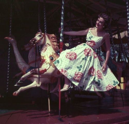 A woman is riding the merry-go-round at Batter sea funfair, wearing a floral print sun dress (1955) 