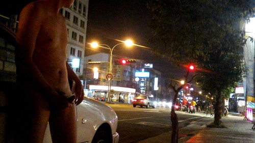 A naked Asian man shows off his hard cock, and masturbates, near a busy city intersection!