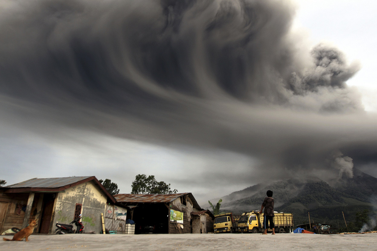 From The Eruptions of Mount Sinabung, one of 19 photos. A woman looks on as Mount Sinabung spews ash, viewed from Sibintun village in Karo district, Indonesia’s north Sumatra province, on November 18, 2013. Mount Sinabung continued to spew volcanic...