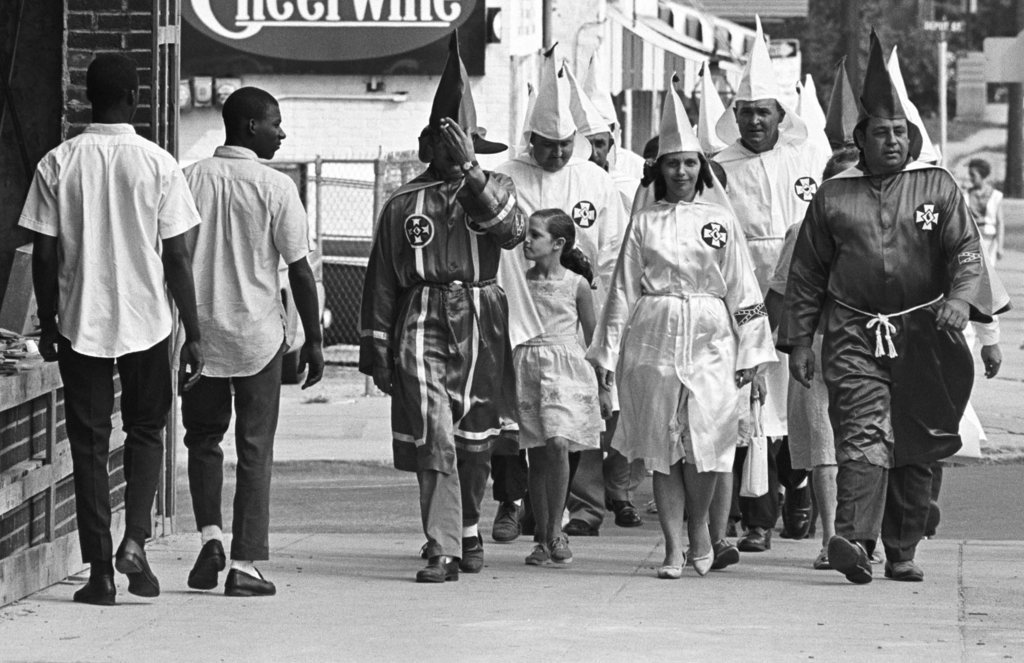 historynet:  Two young black men pass Ku Klux Klan marchers in downtown Salisbury,