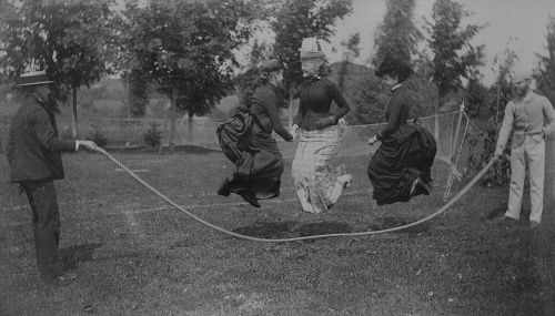 Three women skipping in bustle dresses and of course no lady would be seen without her hat.  Taken c