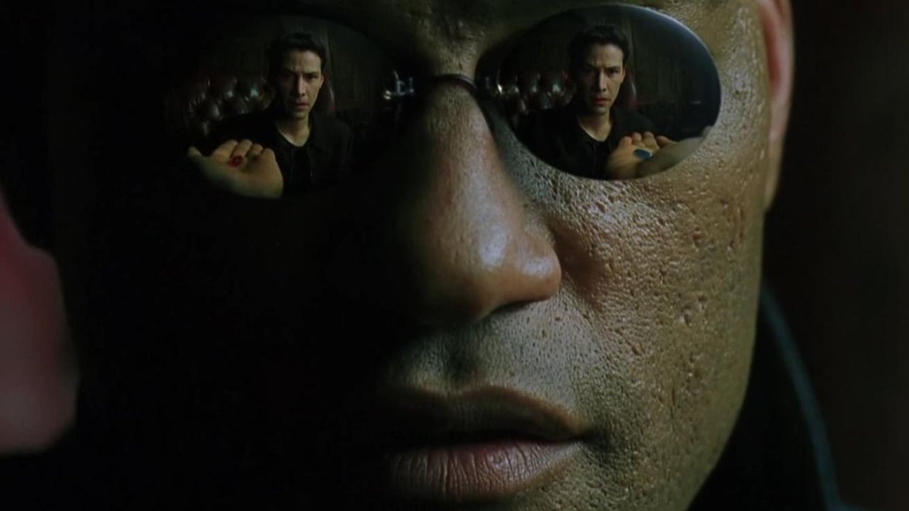 Cena de “Matrix”: um plano fechado do rosto de Morpheus, com o reflexo de Neo, do outro lado da mesa, refletido em seus óculos escuros.