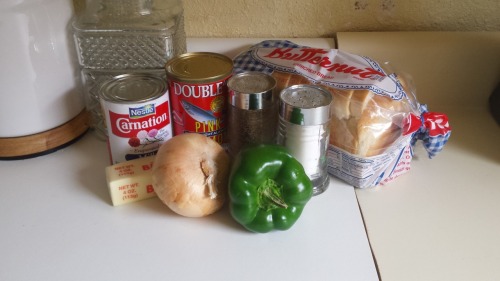 Ingredients on a countertop, including canned milk, butter, onion, green pepper, salmon, salt, pepper, and bread.