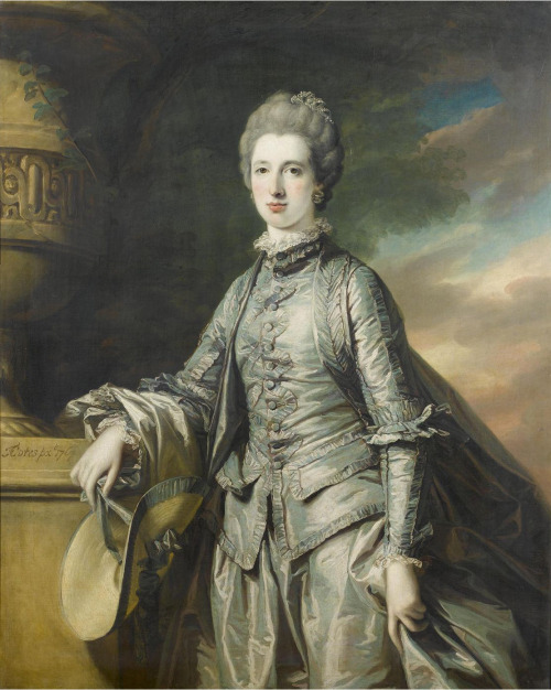 Elizabeth Burdett standing three-quarter-length, in a blue dress, holding a bonnet in her right hand