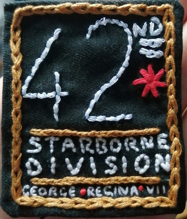 An embroidered patch which reads 42nd Starborne division in large letters. Underneath, smaller text reads 'George Regina VII'. The patch is edged with gold chain stitch