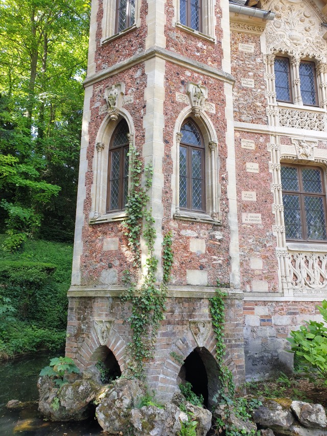 a view of the tower, showing how it stands on artificial rocks on a pond with ivy growing over it