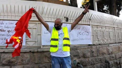 A Palestinian Christian sports a victory sign as he holds a burning Turkish flag outside the Turkish