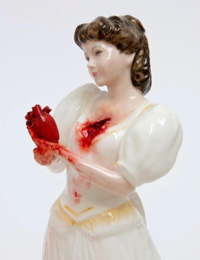 a porcelain doll holds her own bloody heart which she has pulled out of herself