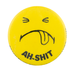 a yellow pin with a face sticking its tongue out and black text reading 'AH-SHIT'