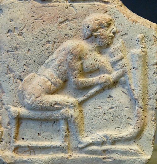 Ancient Mesopotamian terracotta relief depicting a worker using an adze to cut a piece of a chariot.