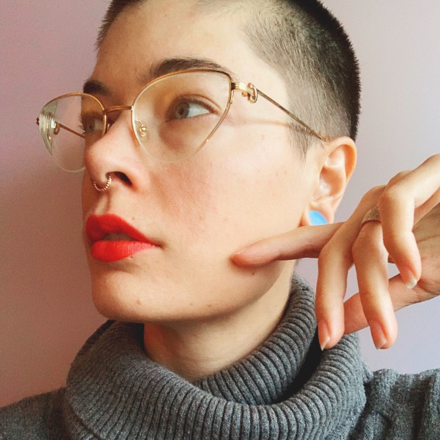 self portrait of artist with shaved head in red lipstick and gold glasses