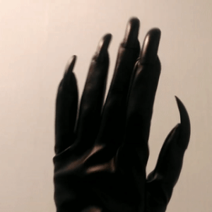 someone holding their hand to the camera, wearing a leather glove with black claws. their fingers bend and shift