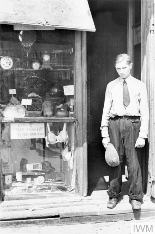 A young man standing in a shop doorway in the Warsaw Ghetto (1941). He has taken off his hat to comp