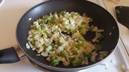 A frying pan of diced onion and green peppers, sautéing in butter