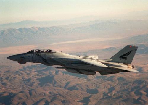 planesawesome:  US  Navy left side view of an Grumman F-14B Tomcat aircraft of Fighter  Squadron 143 (VF-143) the Pukin’ Dogs in flight over desert terrain ,  Nevada . Scene Camera Operator: LT. Jack Liles