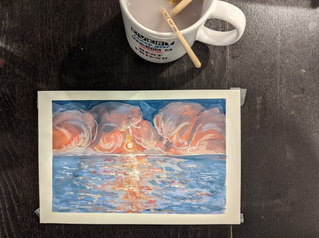 A picture of a painting of a pink ocean sunset. A mug full of water with paintbrushes sits in the corner of the image. 