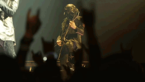 Phantom Ghoul rocks out, playing guitar behind Papa on stage. He wiggles his head side to side.
