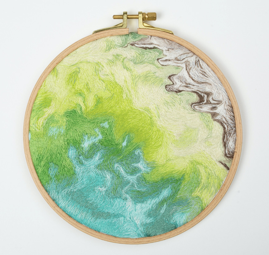 This image shows an embroidery piece inspired by NASA imagery. The background is white. In the middle, a brown frame appears holding an illustration of the Caspian Sea. To the bottom left, blue, green and light green sea appears showing water moving. To the top right, ice gouges are designed in brown and white.
