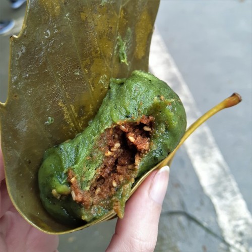 Green glutinous rice ball wrapped in a leaf with some kind of sweetish filling I was unable to ident