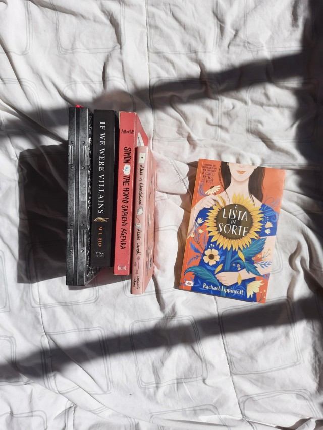 the Drowning Girl, if we were villains, Simon vs the Homo Sapiens Agenda, alice in Wonderland placed together in a row, showing the spines. the lucky list is flat in the white blanket. the sun light is creating spaces of light and shadow