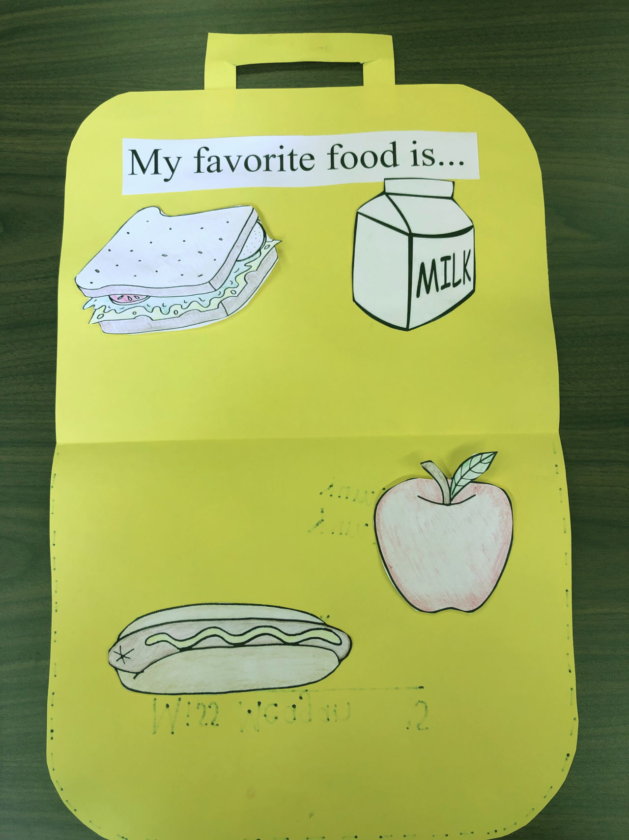 The lunchbox unfolded with "My favorite food" written at the top and a cut out of a carton of milk, a sandwich, an apple, and a hot dog