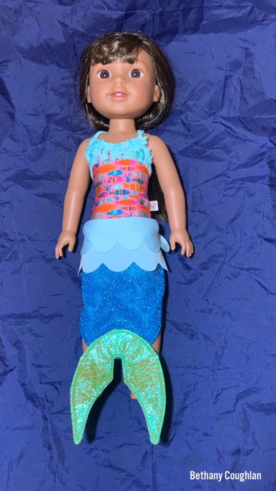 a doll dressed as a mermaid lying against a blue background 