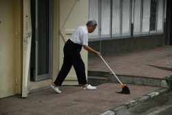 Old man cleans up his driveway with a broom. Bandung, Indonesia.