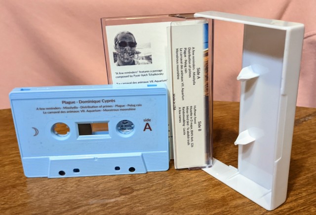 Baby blue cassette with brown-on clear shell labels standing in front of an open clear-and-white Norelco case with J-card.
