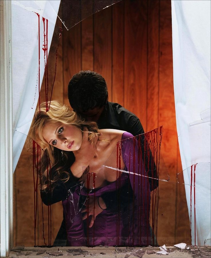 Actress sarah michelle gellar in a purple dress is propped up in broken window with blood spatter. A masked man is holding her from behind.