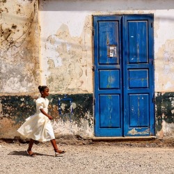 forafricans:  A young girl walks past a blue door in Assomada. Santiago Island, Cape Verde. ©Kuchnia nad Atlantykiem