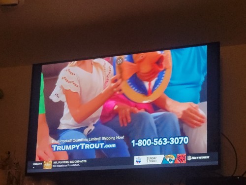 ID: Another photo from the ad showing people sitting together while one of them holds the Trumpy Trout. All faces are outside the frame. End ID.