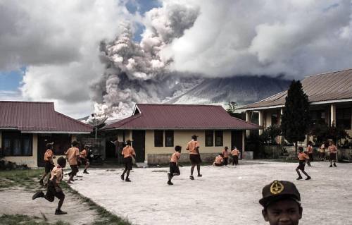 Elementary school children play outside of their classrooms as the Mount Sinabung volcano spews thic