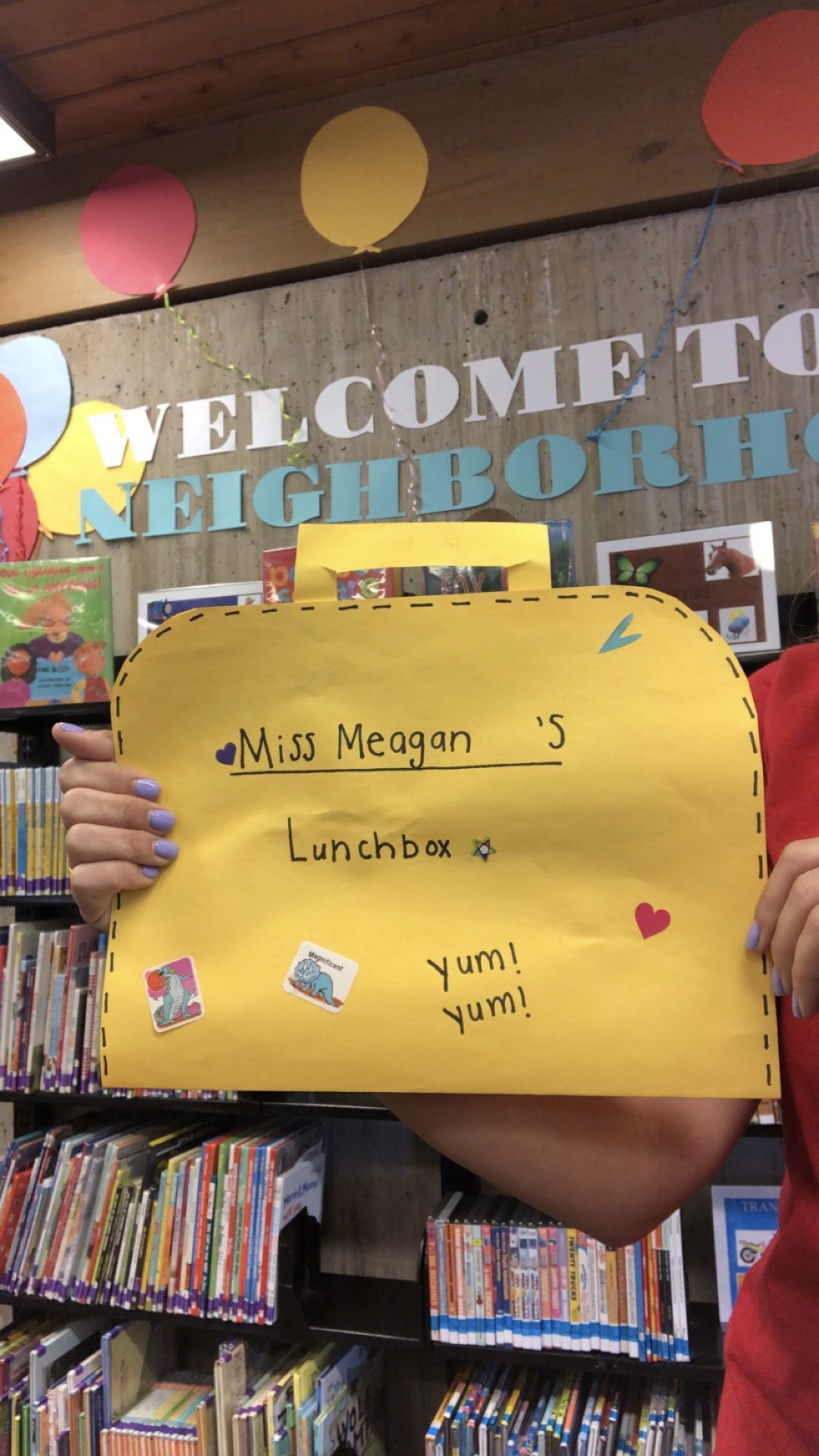 Miss Meagan holds up a large yellow paper lunch box decorated with stickers and her name