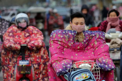 People wear special jackets to keep out the wind while riding on a cold day in Lianyungang, Jiangsu,