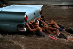 fotojournalismus:  Young people grip on to the bumper of a car in a flooded street in  Havana, Cuba on October 14, 2015. (Ramon Espinosa/AP) 