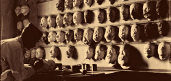 Un artiste travaille sur un masque pour un soldat blessé ayant des blessures au visage face à un mur de moulages de visages d'autres soldats blessés, Paris, c. 1918. An artist works on a mask for a wounded soldier with facial injuries in front of a